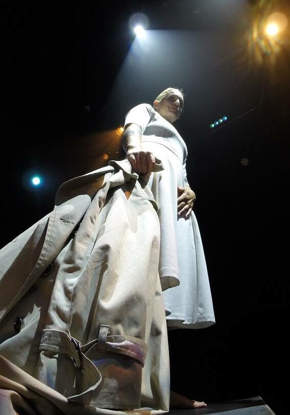 Lady in a white dress holding a jacket on stage.